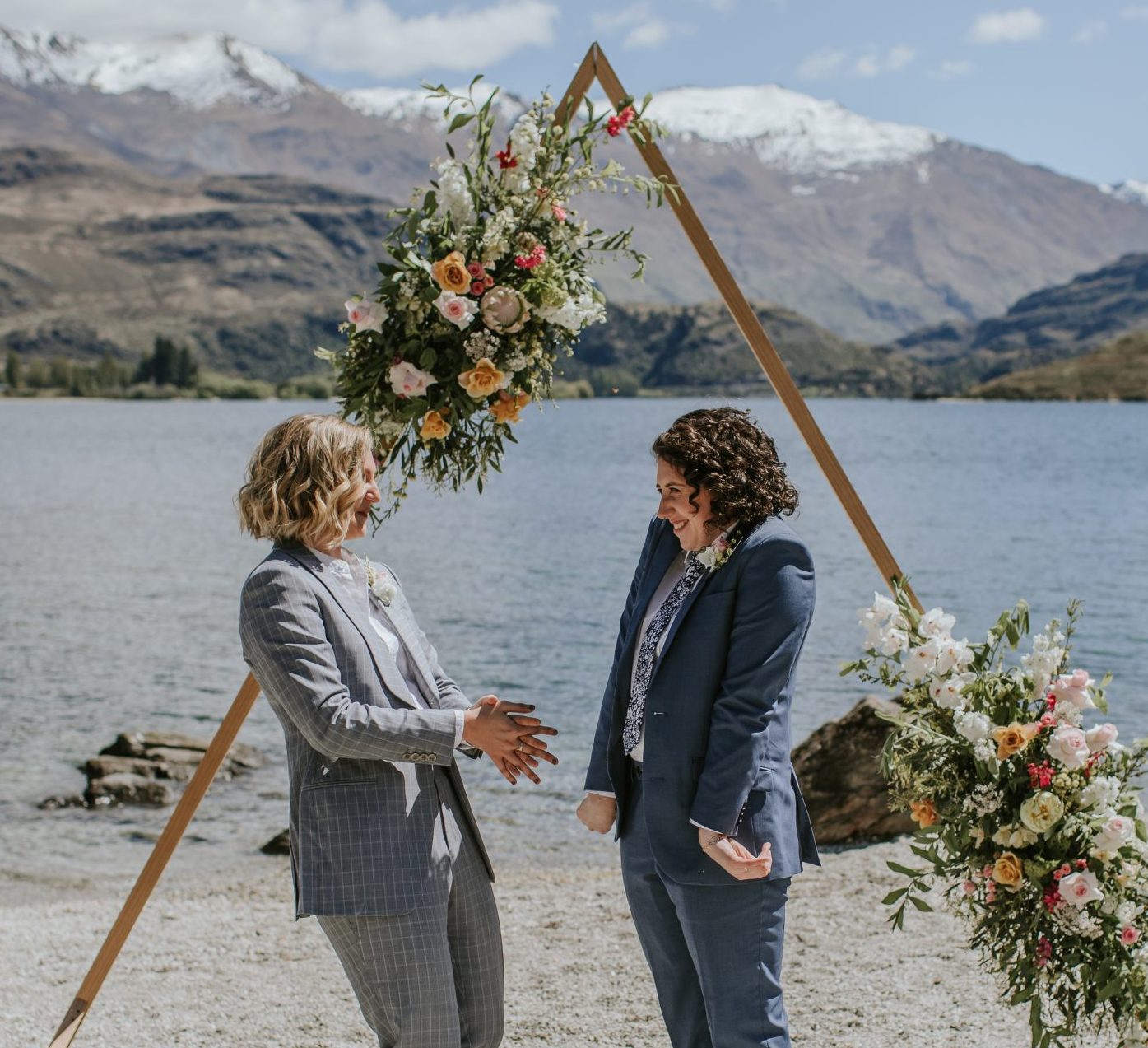 Same sex marriage elopement Glendhu Bay, Wanaka New Zealand, Marriage celebrant Siobhain laughing with wedding arch, Lake Wanaka and Mount Aspiring in the background
