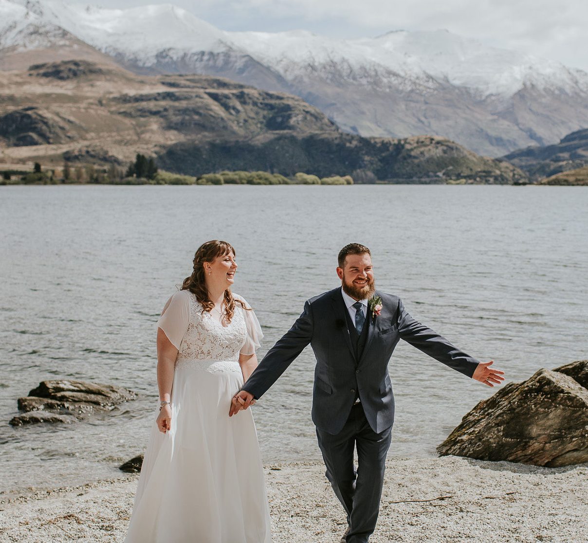 Wanaka small wedding at Glendhu Bay, wedding by Wanaka marriage celebrant, Siobhain the Celebrant, couple smiling and laughing taking a bow with Lake Wanaka in background and snow capped mountains