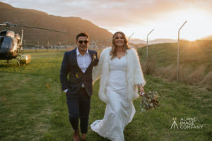 Groom and Bride walking at sunset with helicopter and mountains behind them