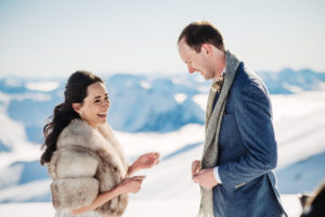 Bride and groom surrounded by snow and mountains laughing during ceremony