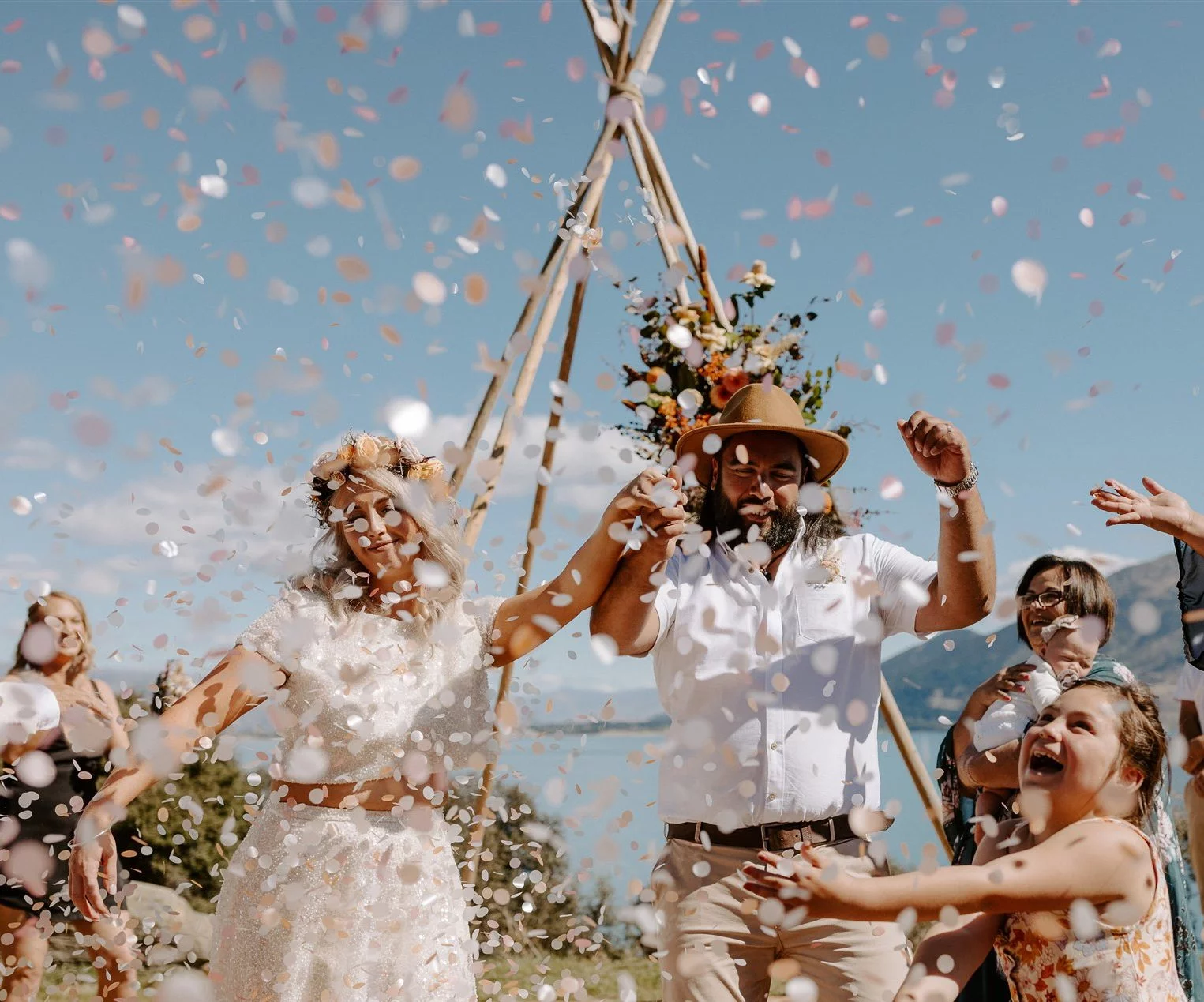 Bride & Groom walking hand in hand through confetti thrown by young girl. Lots of smiles